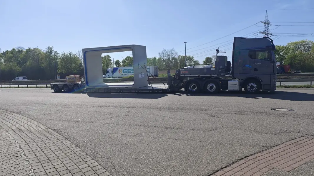 LKW mit einem Tiefbett-Auflieger, auf dem ein großes Betonfertigteil verladen ist.