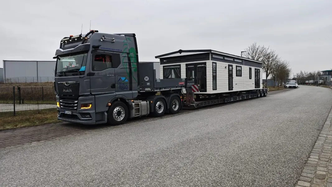 LKW mit einem Tiefbett-Auflieger, auf dem ein Mobilheim verladen ist.