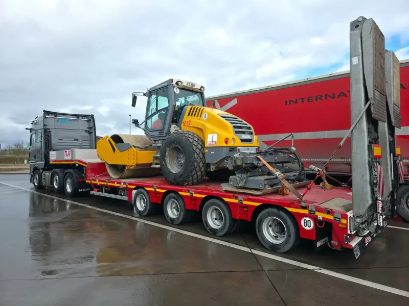LKW mit einem Semi-Tiefbett-Auflieger, auf dem eine Baumaschine verladen ist.
